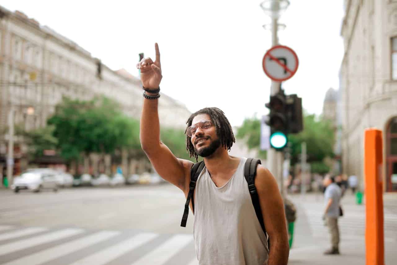 Hombre étnico feliz con mochila parando un taxi en la calle