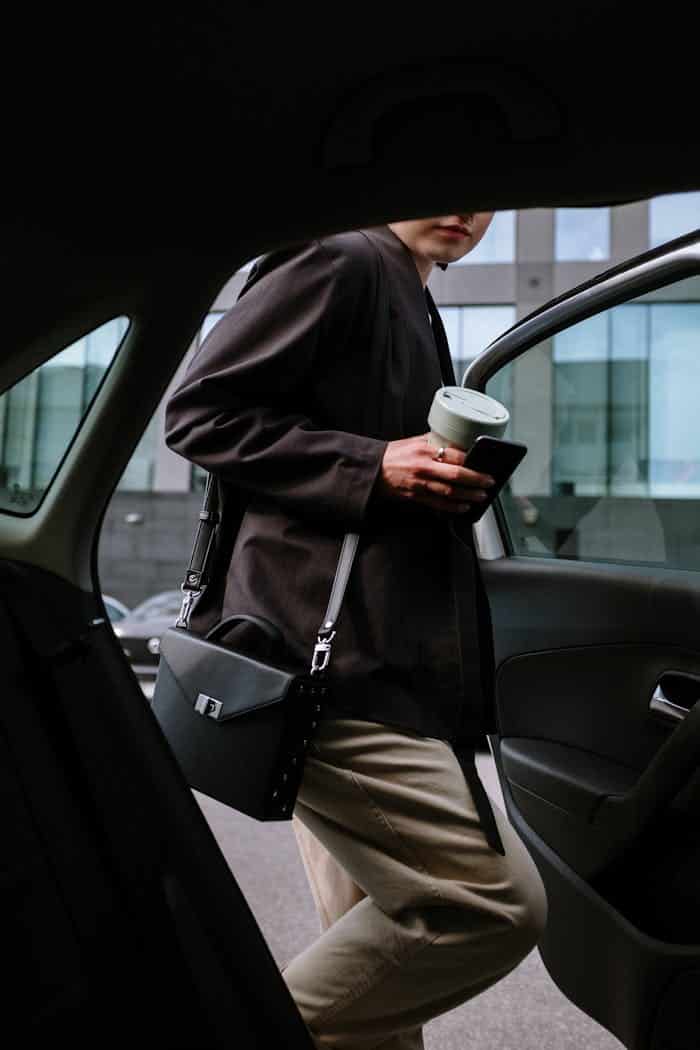 Mujer con abrigo negro sosteniendo taza blanca entrando al taxi