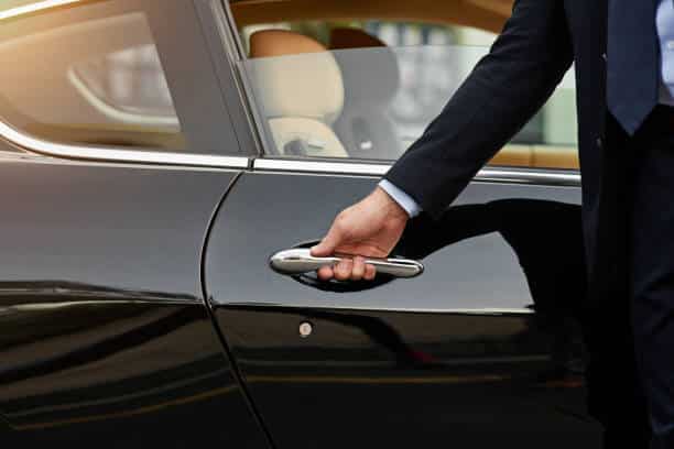 Recorte de un irreconocible chófer masculino abriendo la puerta de un taxi